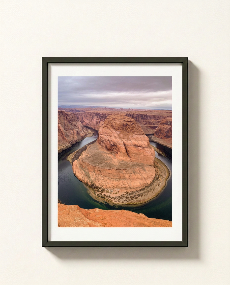 Framed landscape art print of Horseshoe Bend in Arizona, featuring the winding Colorado River around a red rock canyon under a cloudy sky, displayed on a light beige wall.