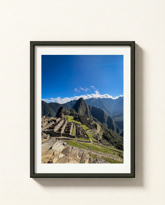 A framed photographic print of the ancient ruins of Machu Picchu under a bright blue sky, displayed on a light beige wall.